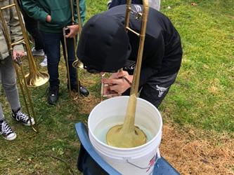 Elementary school student playing a trombone into a bucket of water