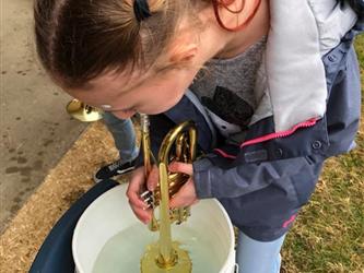 Elementary school student playing a trumpet into a bucket of water